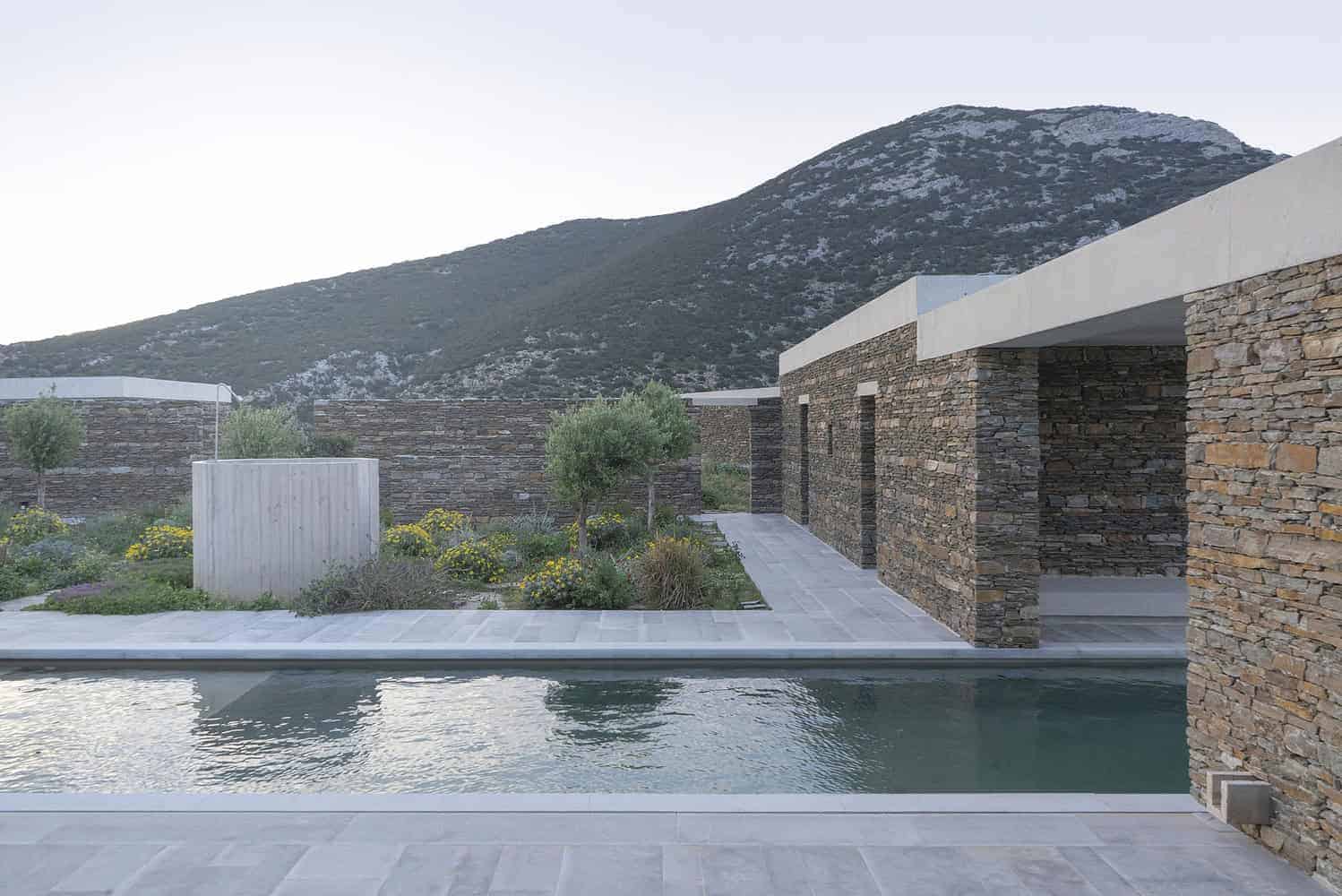 Contemporary modern villa with stone walls, a landscaped garden, and swimming pool set against scenic mountain backdrop, emphasizing minimalist architectural design.