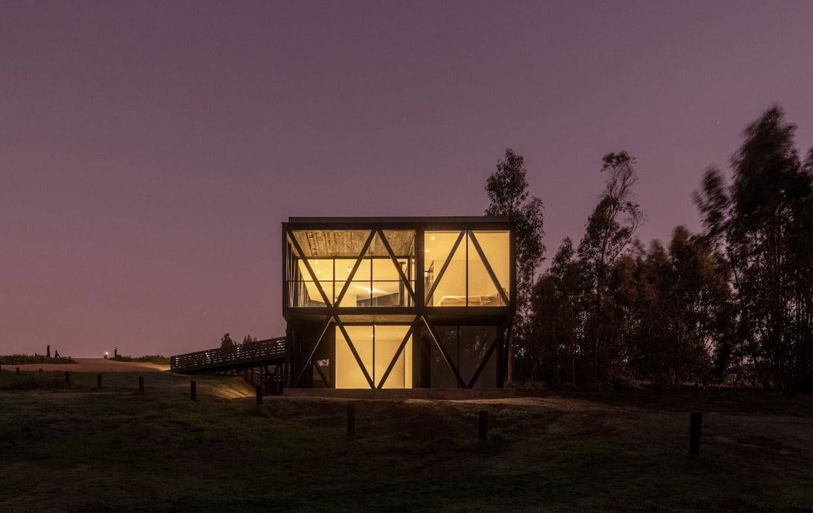 Modern glass house with illuminated interior on a twilight background, showcasing innovative architecture and design.