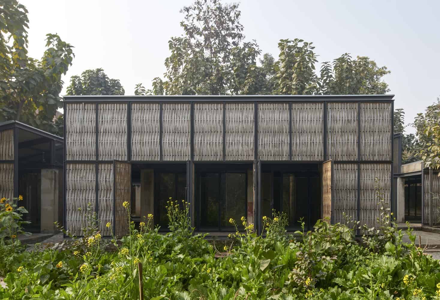 Modern minimalist house with bamboo paneling and large glass doors, surrounded by lush greenery and trees, showcasing eco-friendly architecture and sustainable design.