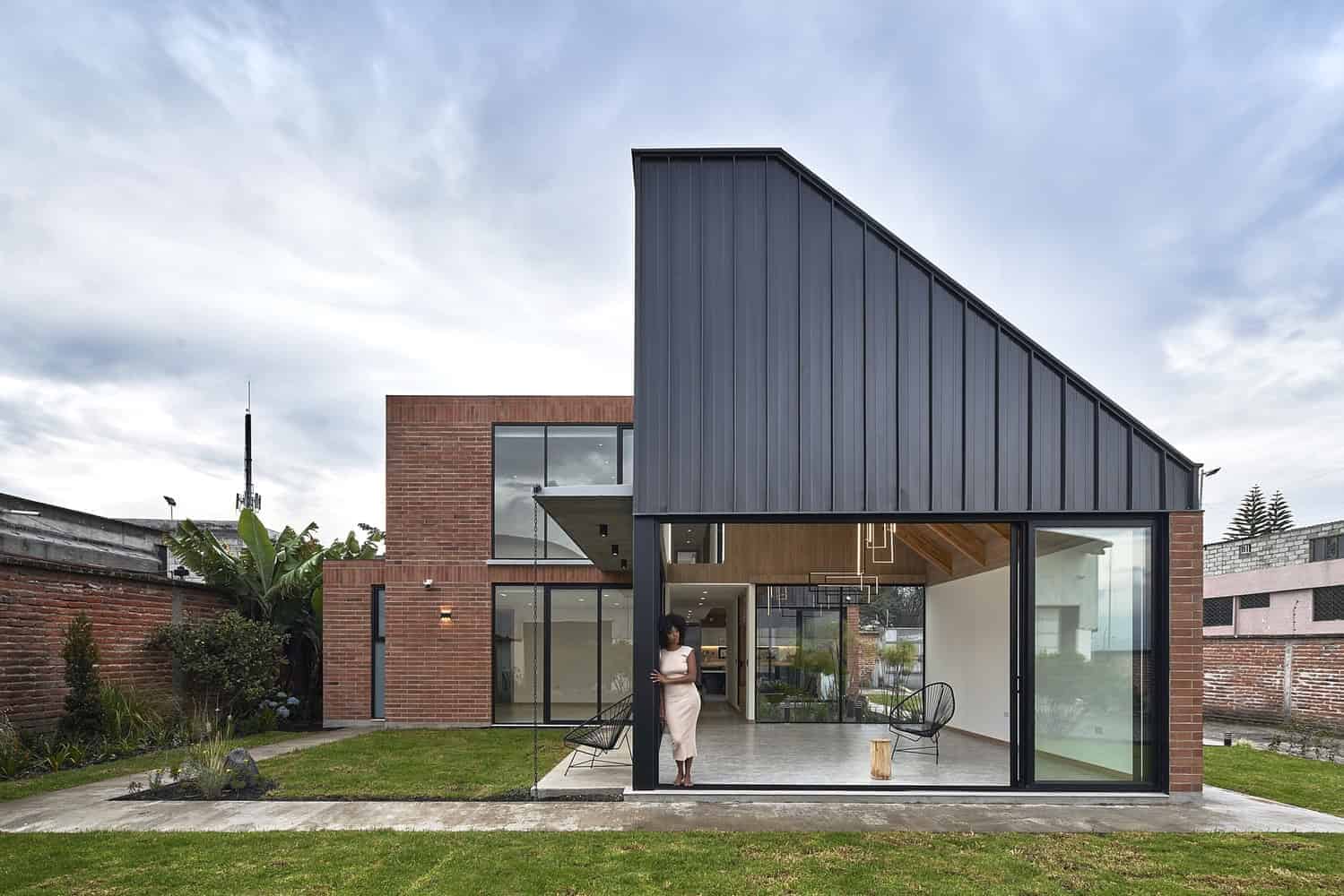 Contemporary modern house with red brick exterior, black metal cladding, large glass windows, and open interior design, showcasing sleek architectural details and modern landscaping.