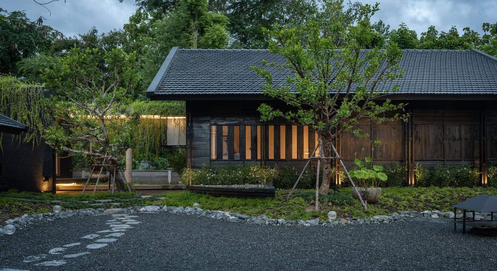 Modern Japanese-style backyard with traditional wooden house, lush greenery, and contemporary landscaping elements.