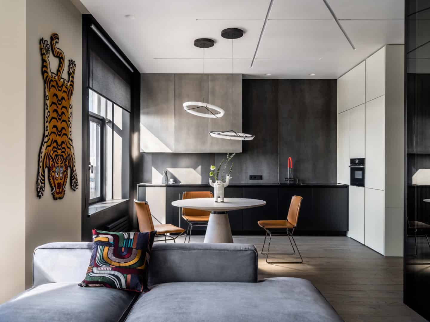 Contemporary minimalist kitchen interior with sleek black and white cabinetry, modern pendant lighting, and a cozy dining area with stylish chairs and decorative accents.