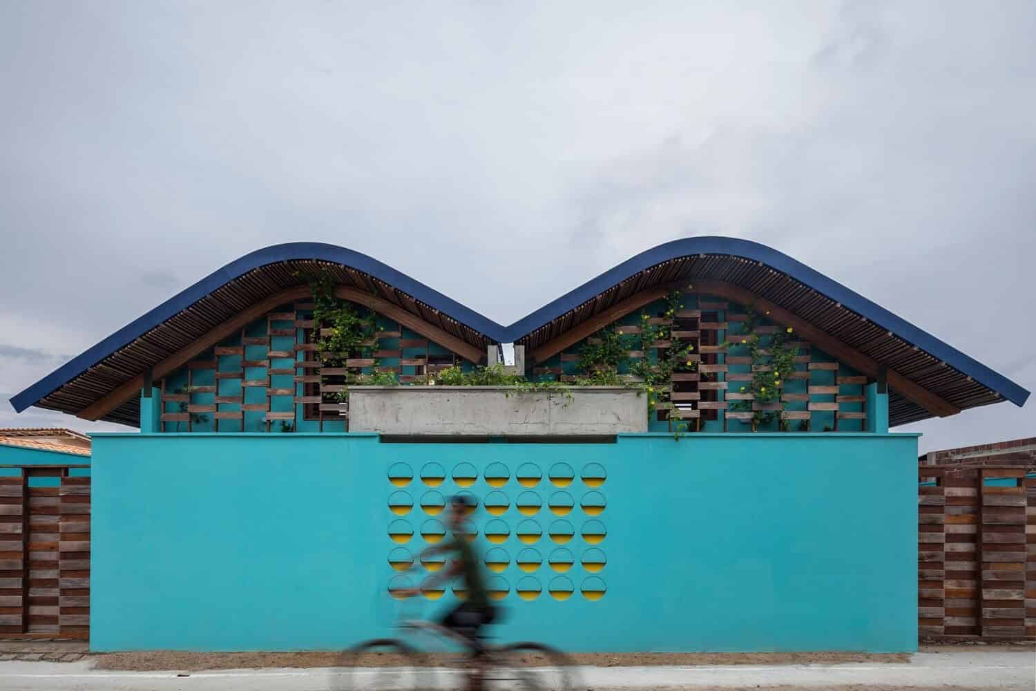 Modern contemporary house with a striking blue facade and unique curved roof design, featuring wooden accents and an eco-friendly rooftop garden, exemplifying innovative architecture and sustainable building practices.