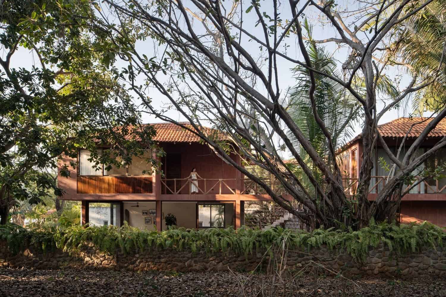 Modern tropical eco-friendly wooden house with large balconies surrounded by lush greenery and mature trees in a serene natural setting.