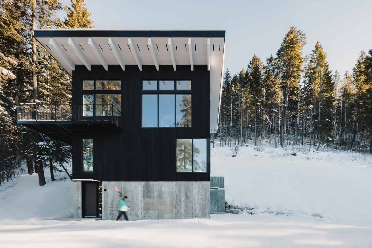 Contemporary black wooden house with large windows in a snowy forest setting, showcasing modern architectural design and innovative use of materials.