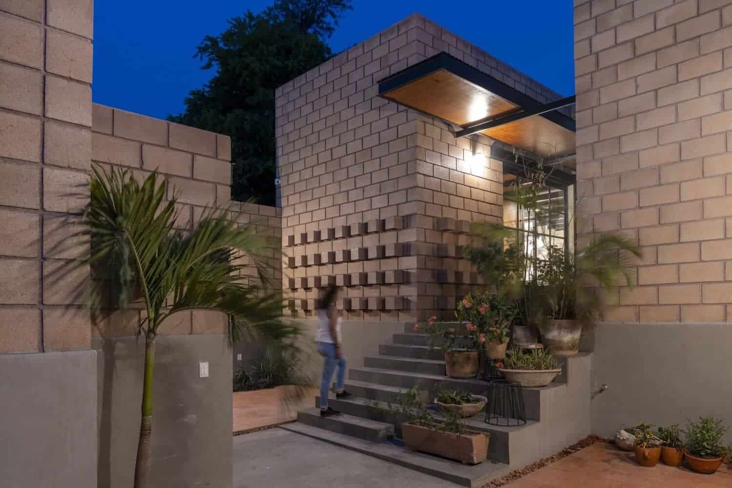 Modern brick house exterior with contemporary architectural design, outdoor lighting, lush potted plants, and sleek stairs at dusk. Perfect for architectural art and innovative home design inspiration.