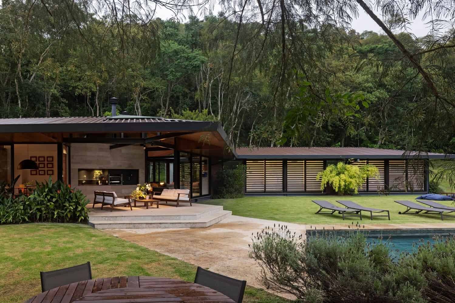 Contemporary modern house with outdoor living area, lush landscaping, and pool in a wooded setting showcasing innovative architecture and stylish outdoor design.