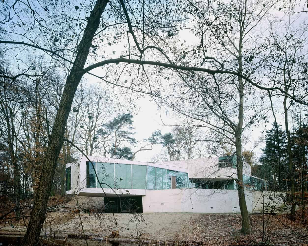 Modern architectural house with extensive glass windows nestled in a wooded forest setting.