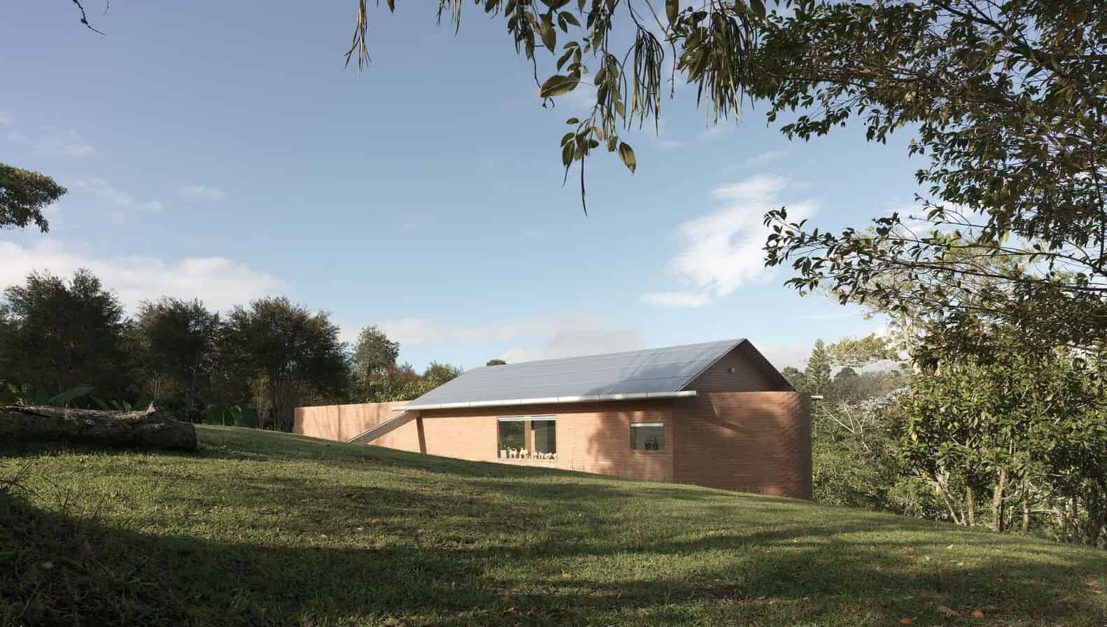 Sustainable modern brick house with metal roof situated in a lush green landscape surrounded by trees and grass.