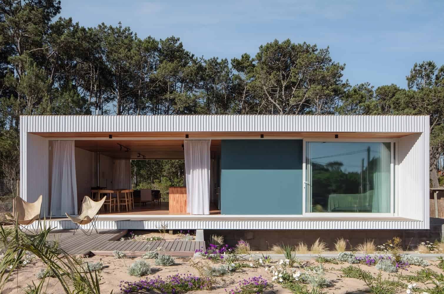 Modern minimalist tiny house with open living space, large glass sliding door, and outdoor patio surrounded by desert and native plants, ideal for contemporary architecture and interior design.