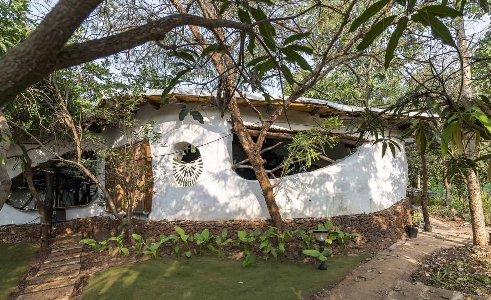 Unique eco-friendly house with organic design blending with natural surroundings, surrounded by lush trees and greenery, showcasing sustainable architecture and innovative construction techniques.