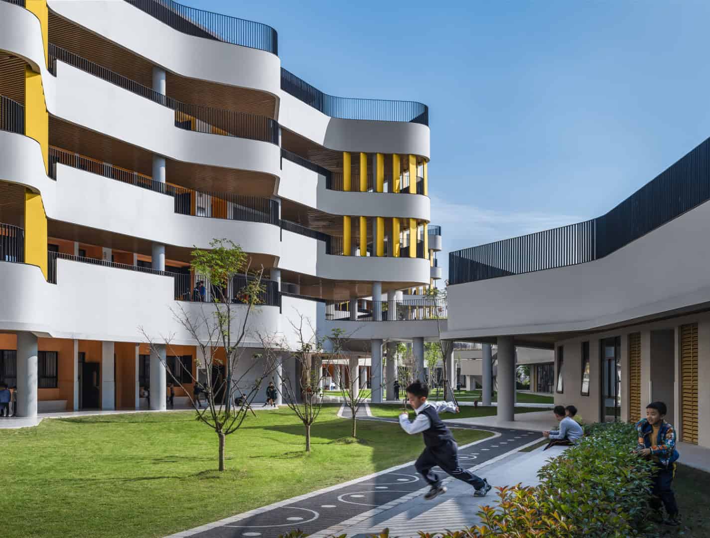 Modern residential apartment building with curvilinear architecture and vibrant yellow accents, surrounded by landscaped green space and children playing, showcasing innovative urban design and contemporary architecture.