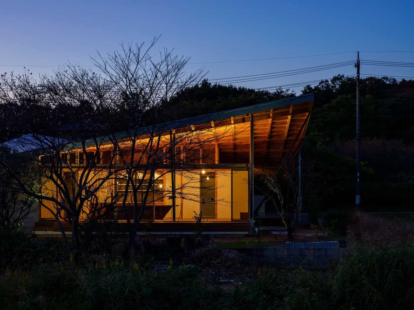 Contemporary modern wooden house illuminated at dusk with sleek architectural design and large glass windows, nestled in a natural setting, highlighting innovative architecture and eco-friendly home design.