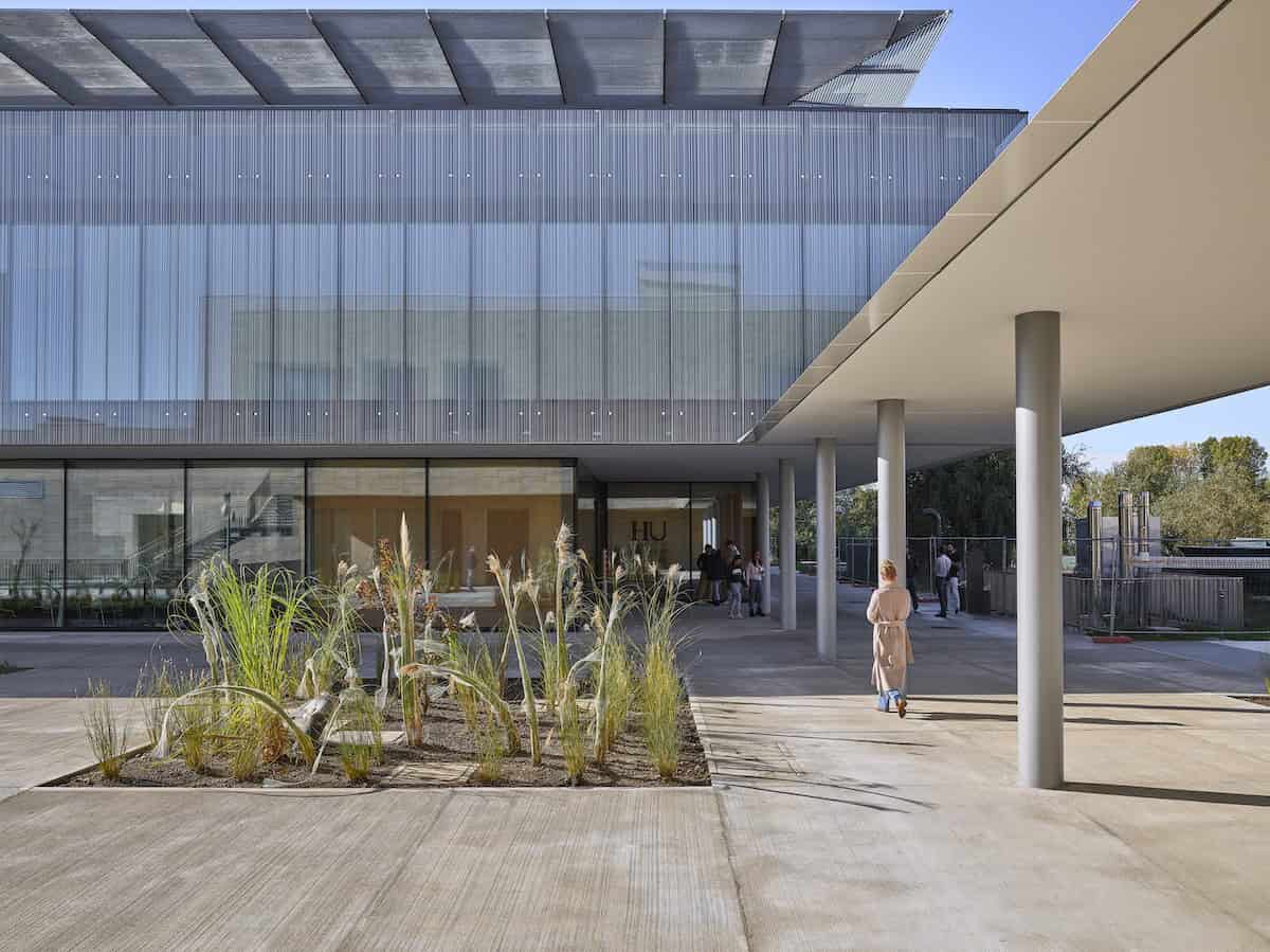 Sleek modern building with glass facade and minimalist architectural design, featuring supporting columns and landscaped greenery, exemplifying contemporary architecture and innovative design.