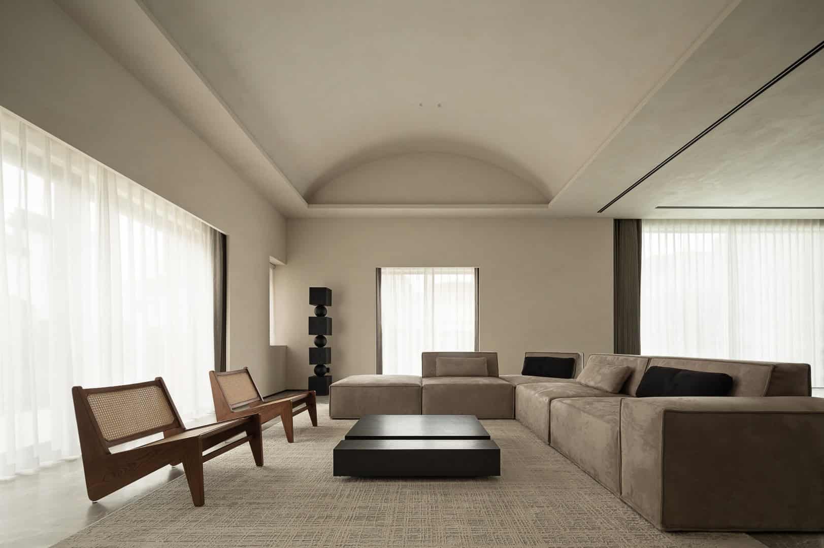 Minimalist modern living room interior with neutral tones, plush beige sofa, wooden chairs, black coffee tables, and large windows with sheer curtains, showcasing contemporary architecture and interior design.