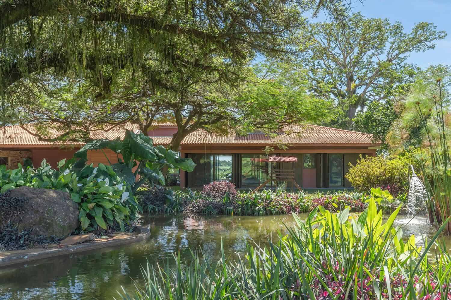 Lush tropical garden surrounding a modern house with a pond, tropical plants, trees, and outdoor water features creating a serene backyard landscape.