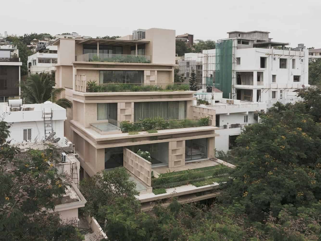 Contemporary modern villa featuring multiple terraces, large glass windows, and lush greenery, situated in an urban hillside with surrounding residential architecture.
