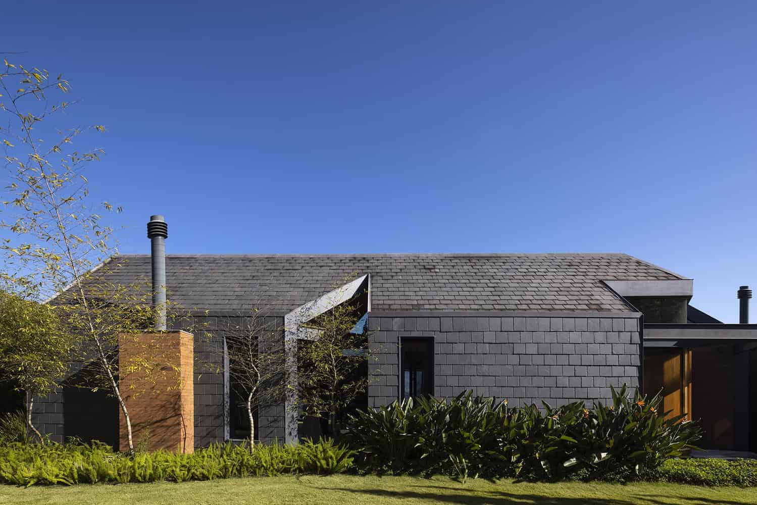 Contemporary modern house with sleek gray brick exterior, minimalist architecture, and lush landscaping under a clear blue sky.