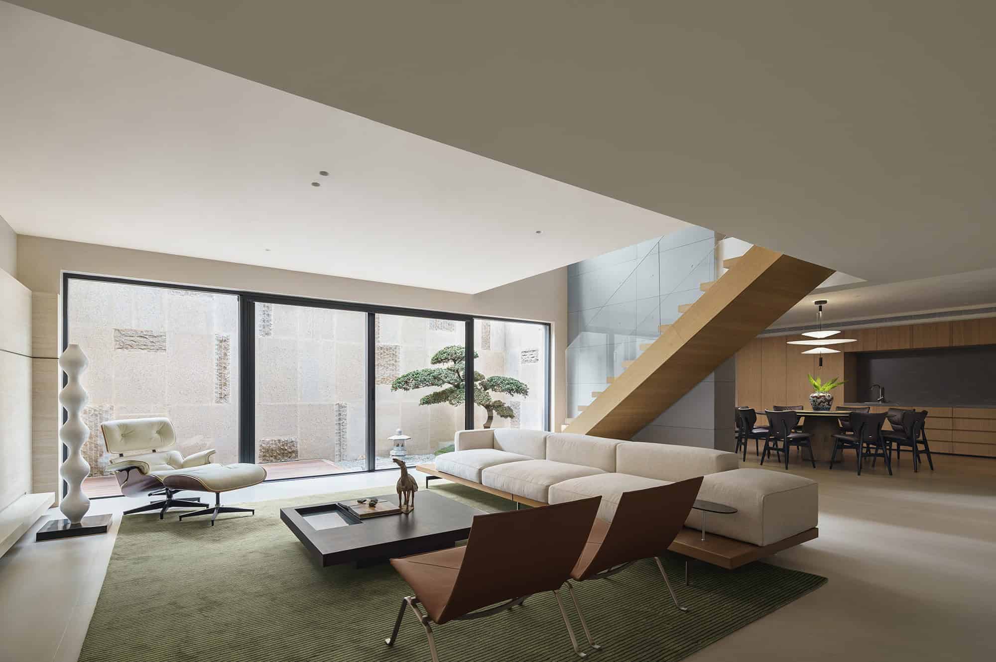 Contemporary modern living room interior with minimalist furniture, large glass sliding doors, and a sleek staircase, showcasing sophisticated architecture and design.