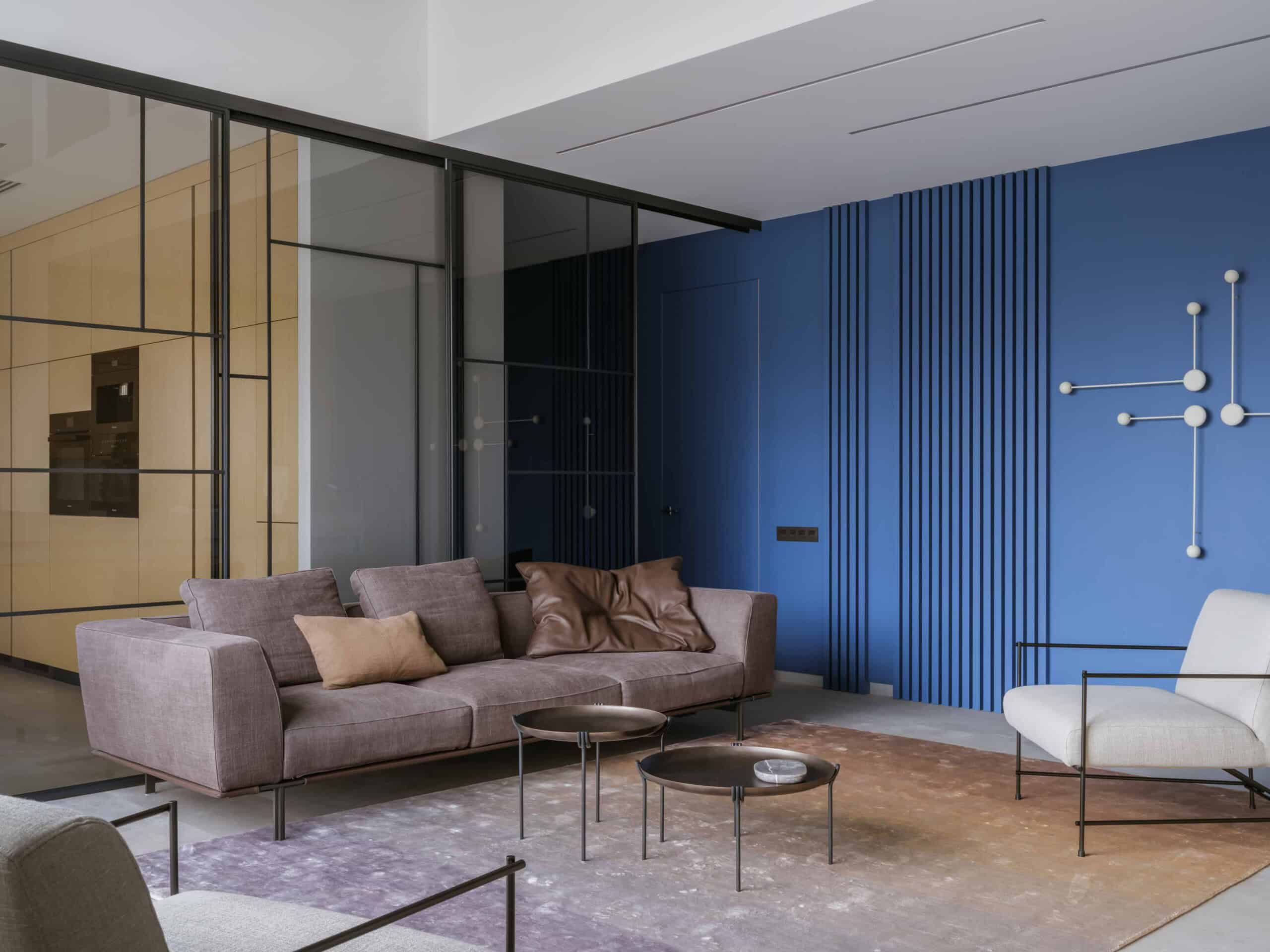 Modern living room interior with a stylish taupe sofa, contemporary armchairs, abstract wall art, and vibrant blue accent wall showcasing modern architecture and design elements.