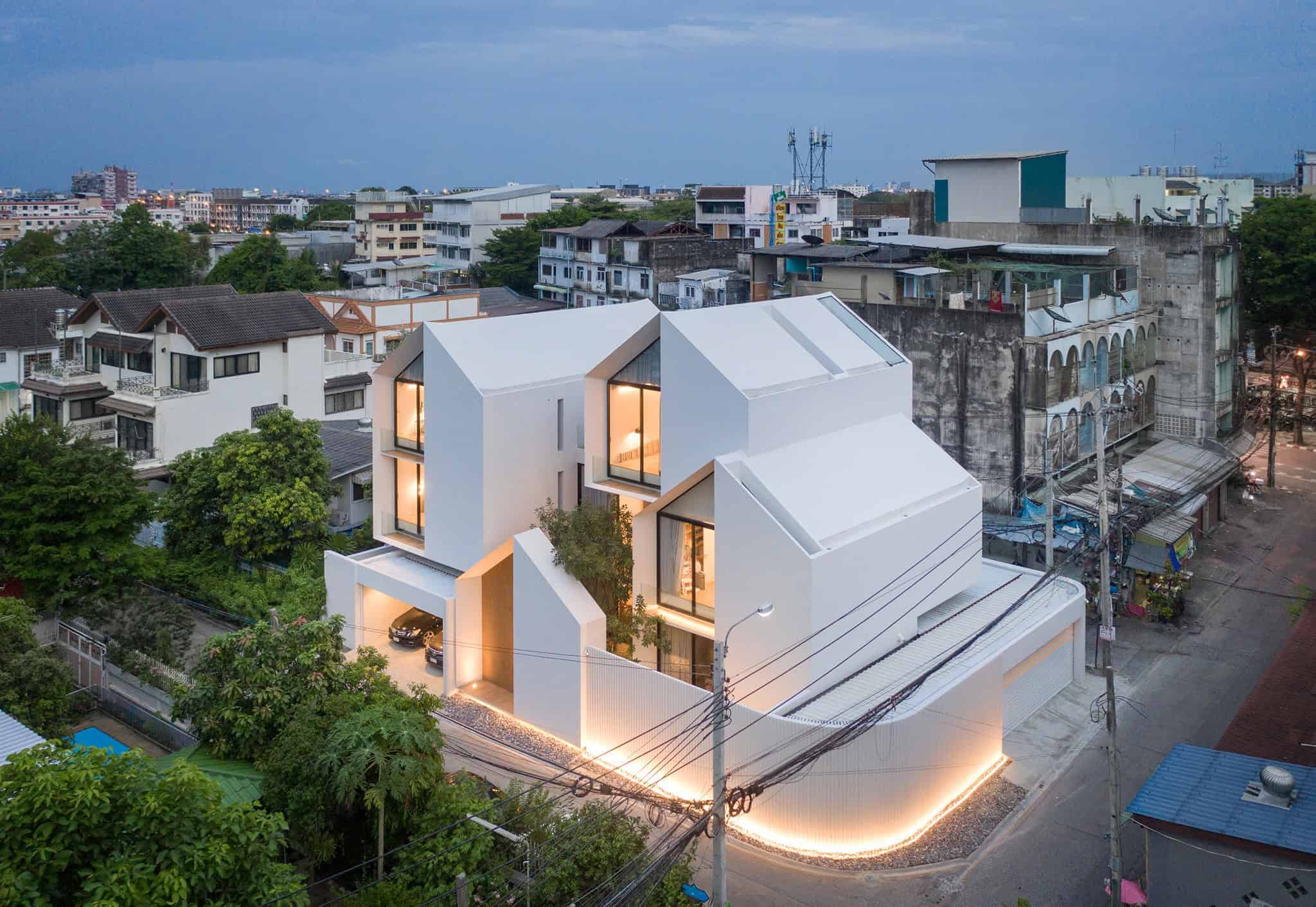 Modern white contemporary residential building with innovative architecture design and large windows in an urban neighborhood at dusk.