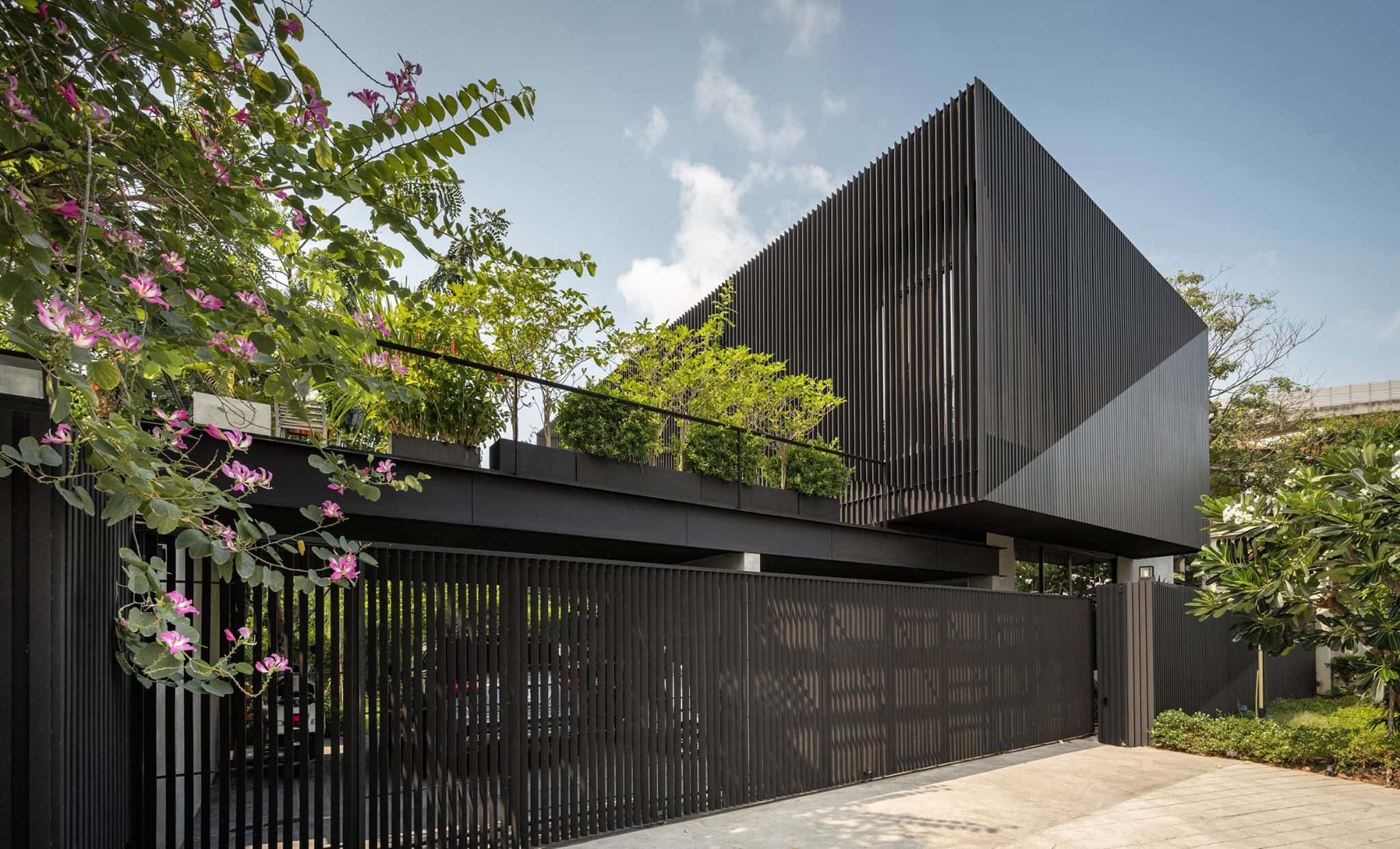 Contemporary black architectural house with vertical slat façade and lush greenery rooftop garden under a clear blue sky.
