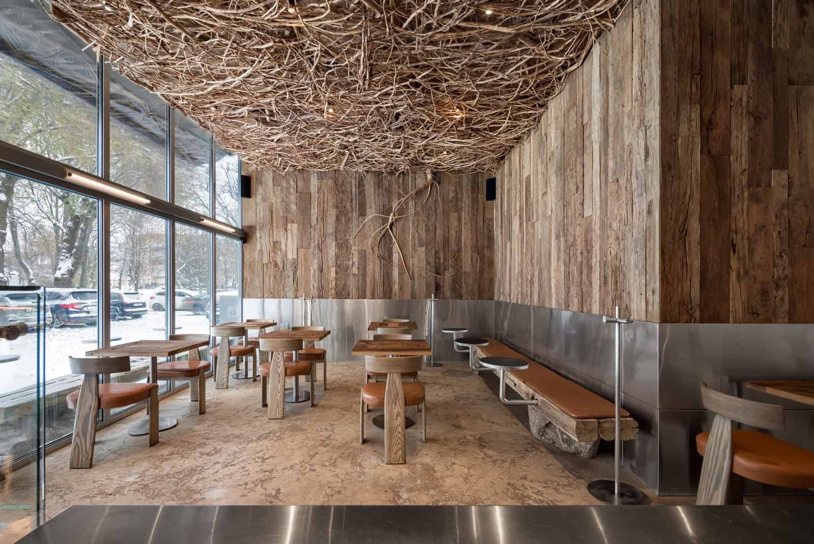 Rustic wood interior design featuring natural wood wall paneling, unique branch ceiling art, and contemporary furniture in a cozy, nature-inspired cafe setting.