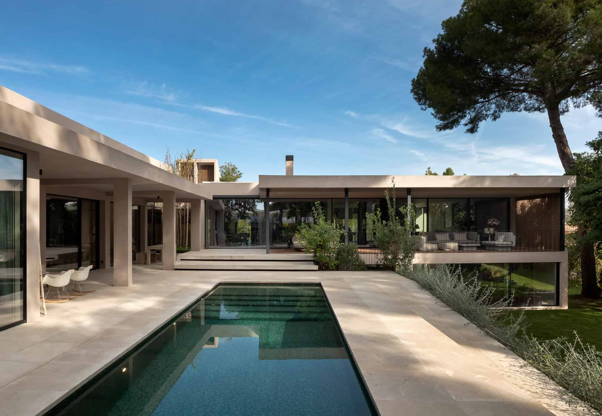 Modern sleek villa with minimalist architecture and large glass windows, outdoor pool, and landscaped garden. Contemporary design emphasizing open spaces and clean lines in a lush natural setting.