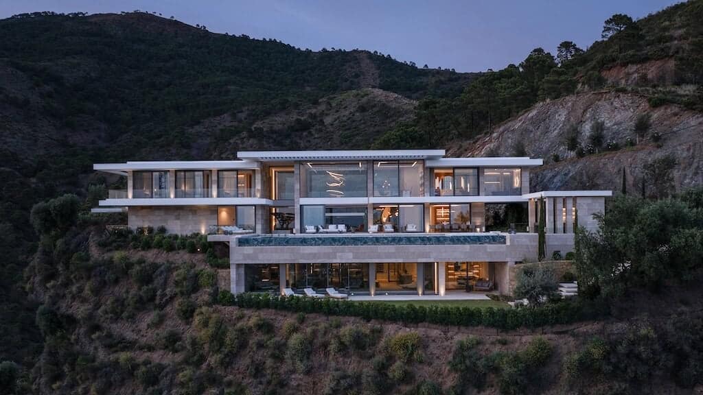 Luxury modern hillside villa with expansive glass walls and stunning mountain views, showcasing high-end architecture and innovative design.