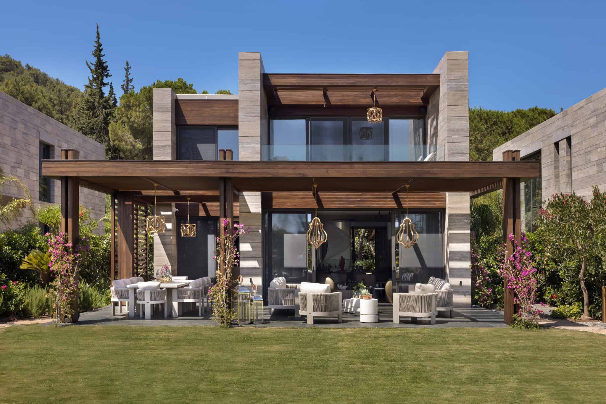 Contemporary modern house with spacious outdoor patio and stylish furniture, surrounded by lush garden and scenic hillside, featuring sleek architecture and an elegant outdoor living space.