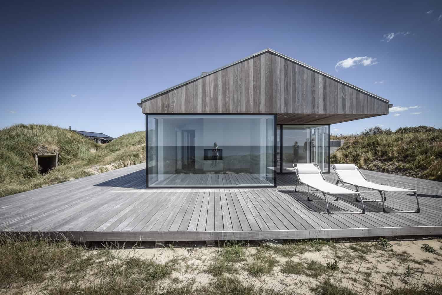 Stylish modern house with glass walls and wooden accents on a scenic beach landscape.