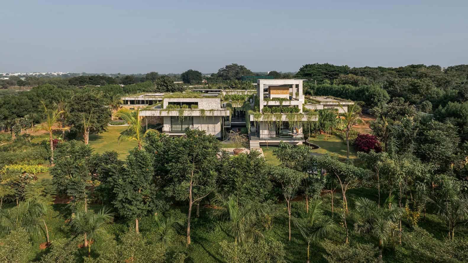 Modern luxury house with sleek concrete architecture surrounded by lush tropical gardens and trees, emphasizing innovative design and sustainable landscaping.