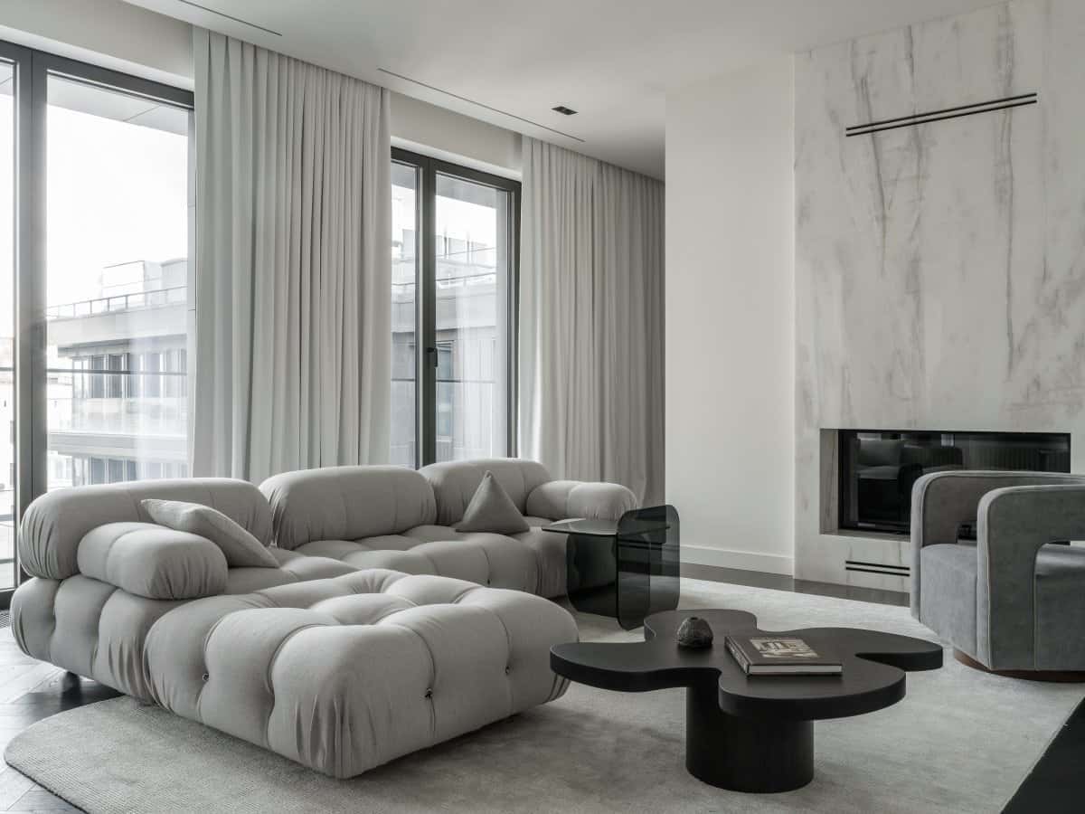 Elegant modern living room with neutral color palette, plush sectional sofa, marble fireplace, large windows with white curtains, contemporary black coffee table, sleek armchair, stylish minimalistic decor, perfect for contemporary interior design. |.