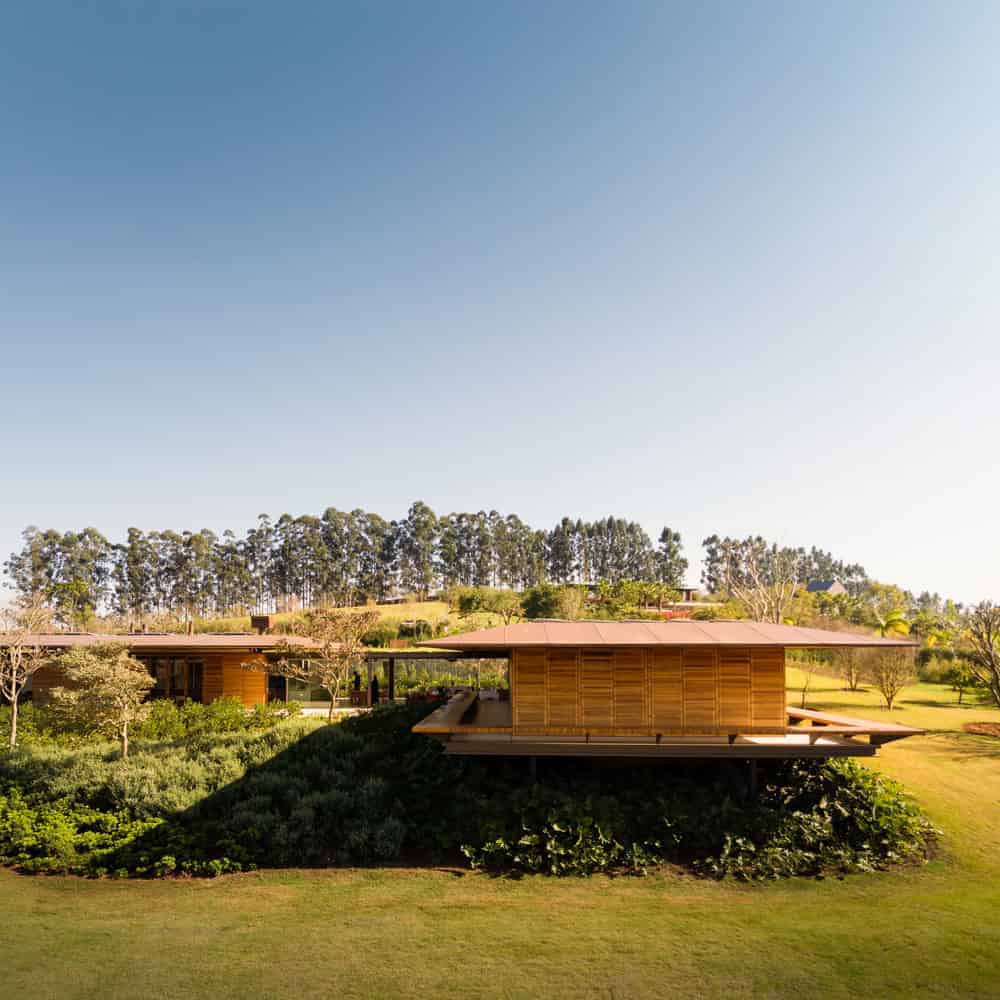 Modern wooden house on stilts with lush green landscape and clear blue sky, showcasing contemporary architecture and innovative design.