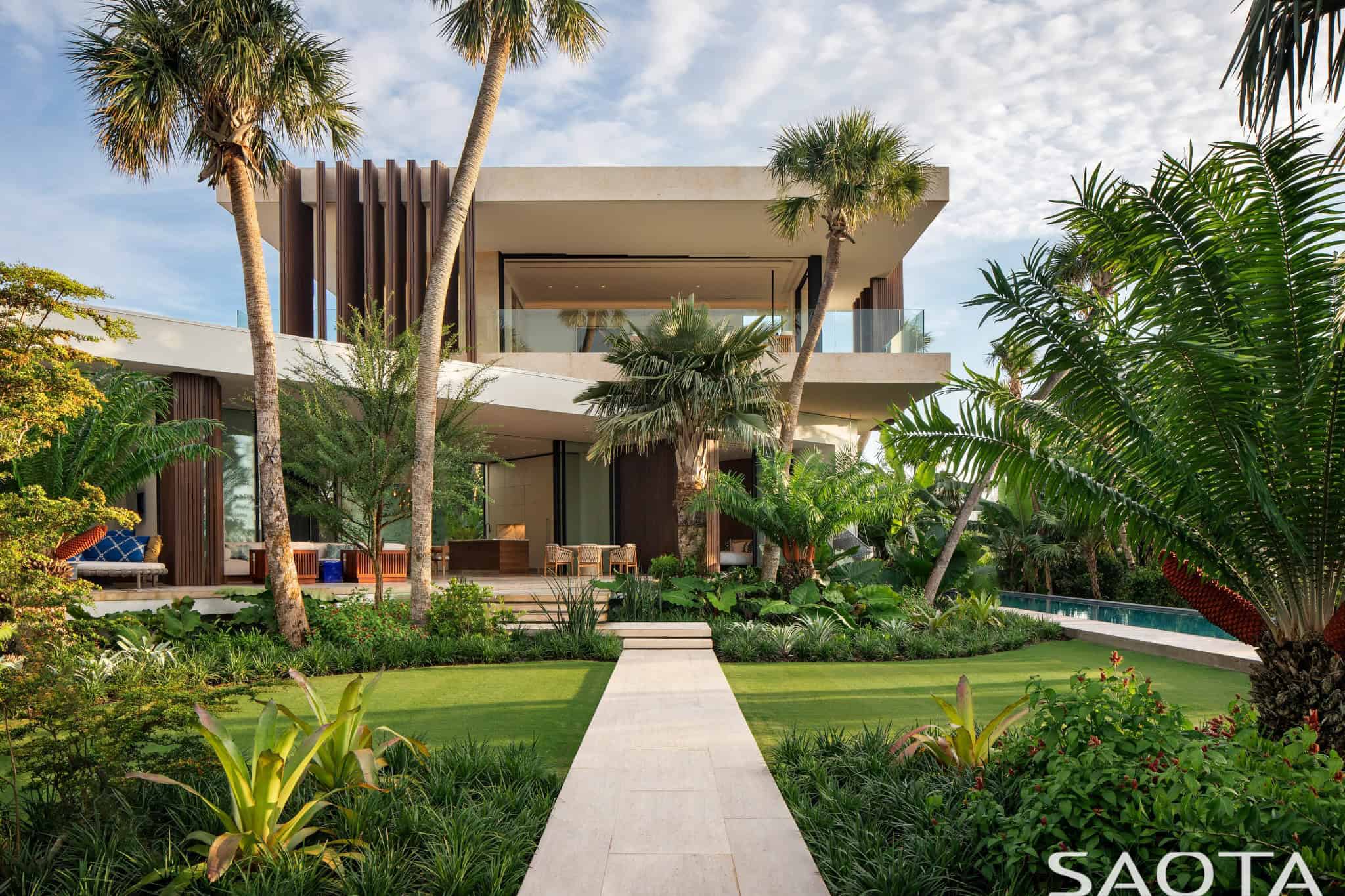Luxurious modern tropical house with contemporary architecture, lush landscaping, and an infinity pool, surrounded by tall palm trees and vibrant greenery for a stylish and serene outdoor space.
