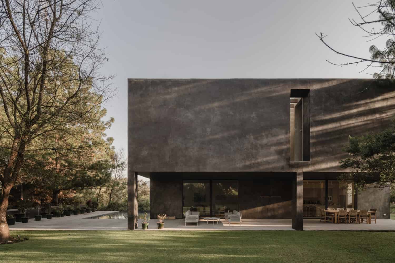 Contemporary modern house with dark concrete exterior, large glass doors, minimalist outdoor furniture, and lush greenery, showcasing innovative architecture and stylish exterior design.