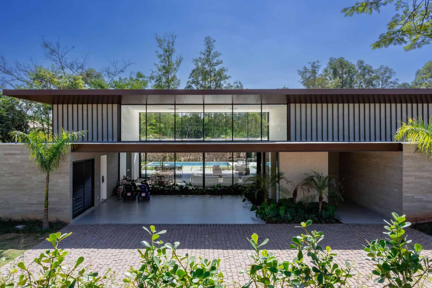 Modern contemporary house with large glass windows, sleek design, and a spacious driveway surrounded by lush greenery. The house features minimalist architecture with clean lines and natural textures.