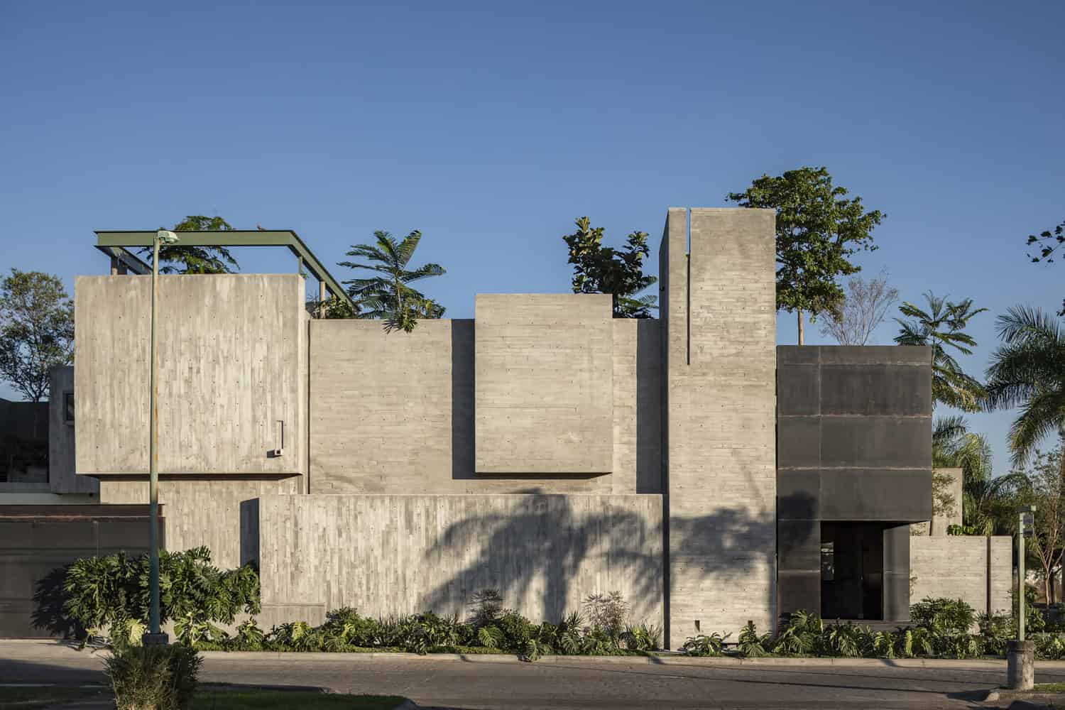 Contemporary concrete building with geometric design and modern architecture elements, surrounded by lush greenery and clear blue sky.