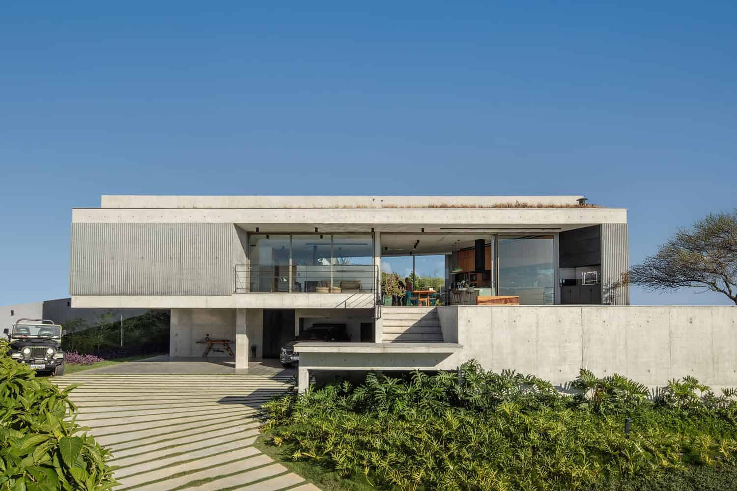 Modern minimalist concrete house with large glass windows, open-plan interior, and sleek design, featuring lush landscaping and a spacious driveway, exemplifying contemporary architecture and stylish home design.