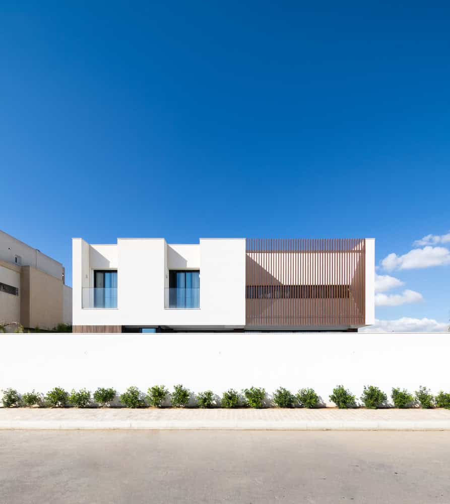 Modern minimalist house with sleek white facade and wooden accents, featuring large windows and contemporary design, under a bright blue sky. Perfect for architecture art designs and modern building inspiration.