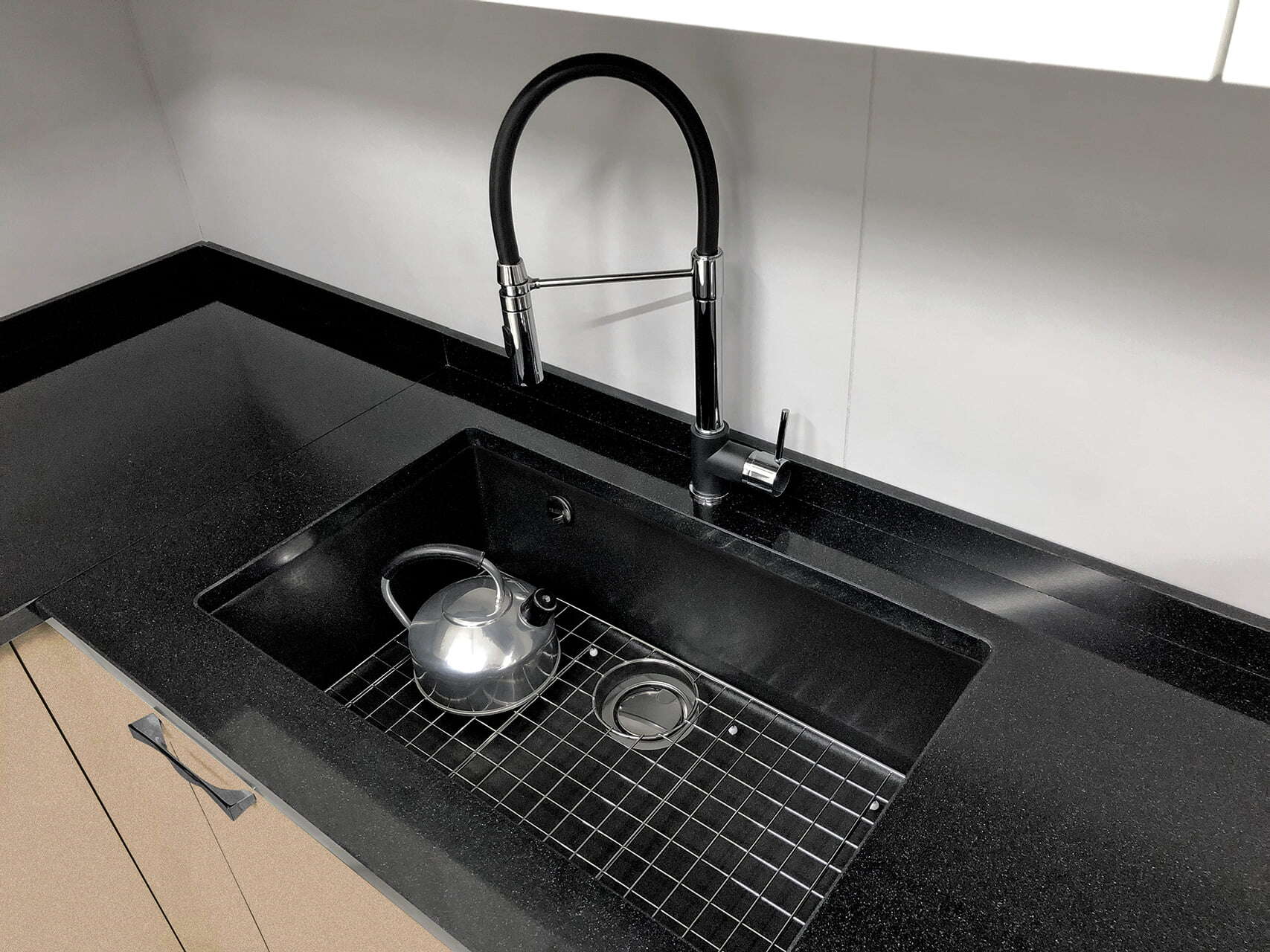 Una griglia fondo vasca GRID84 si trova in un lavello da cucina nero con un rubinetto moderno ad arco alto.