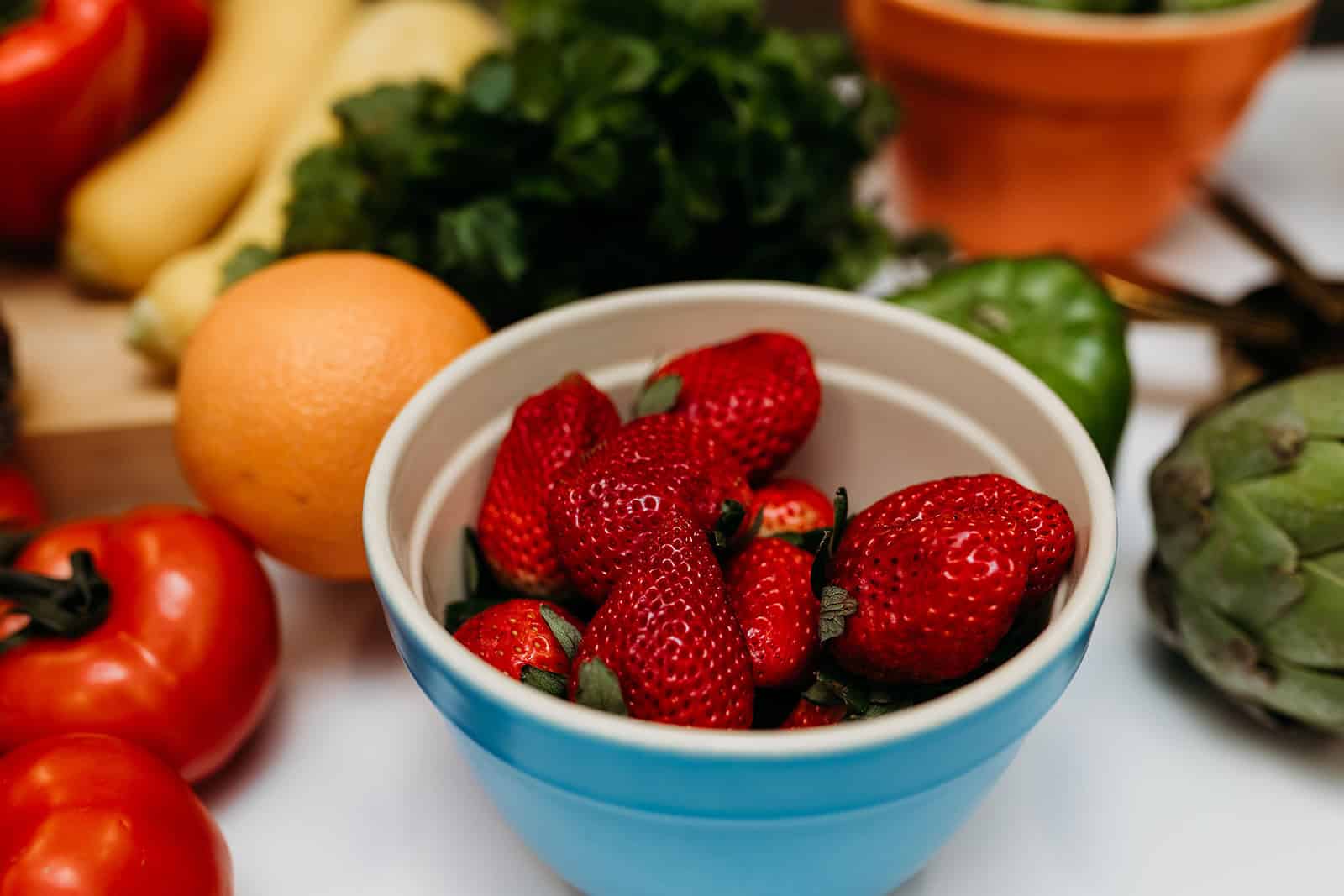 image of strawberries in a blue bowl surrounded by produce