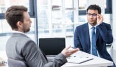 Two businessmen in formal wear sitting and talking at job interview, business concept