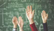 Students raised up hands green chalk board in classroom