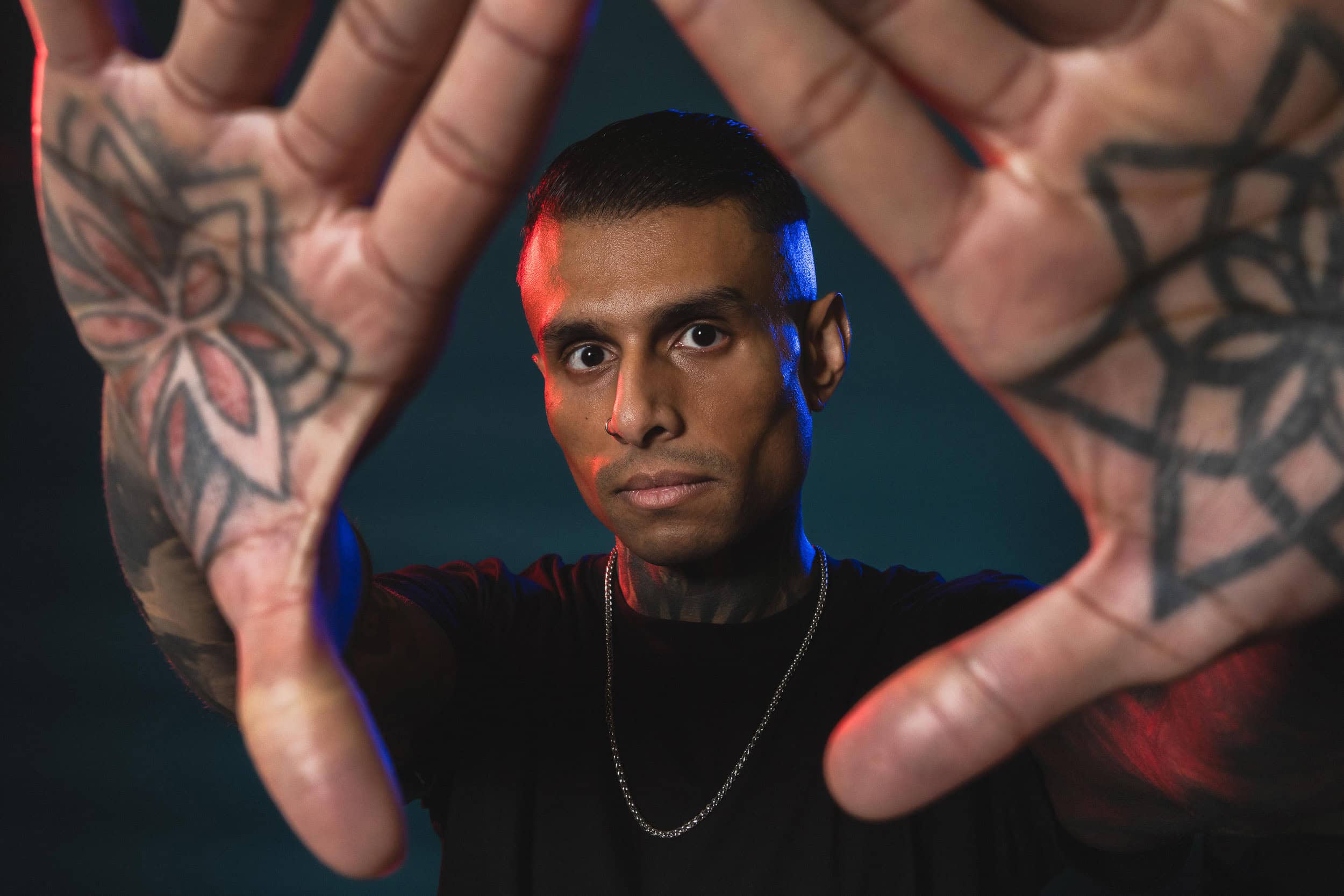 studio-portrait-of-male-with-tattoos-on-hands-and-red-and-blue-lighting