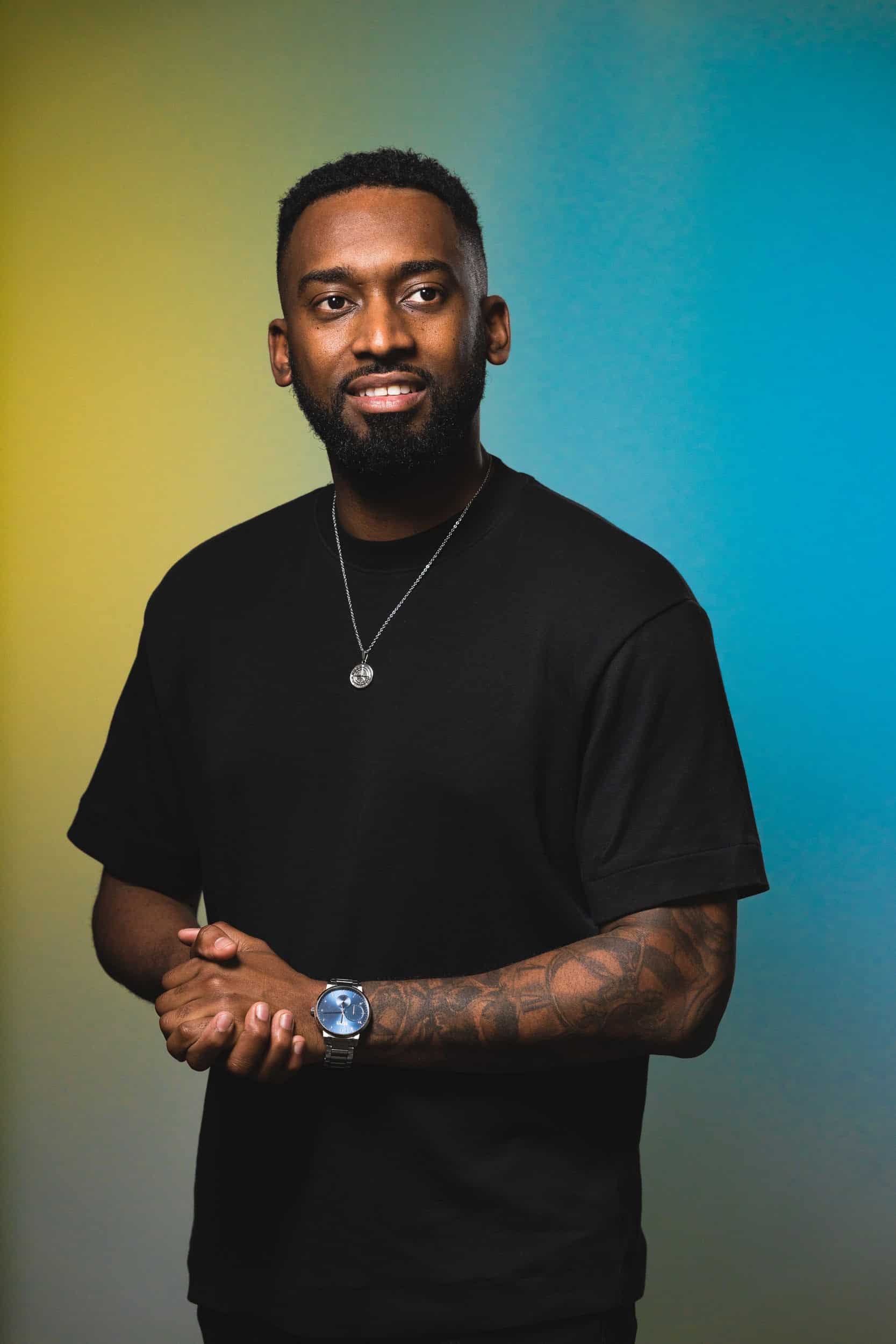 studio-portrait-of-male-with-tattoos-on-arm-and-yellow-and-blue-backdrop