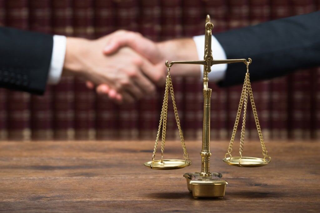 Justice Scale On Table With Judge And Client Shaking Hands business litigation attorney greensboro