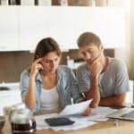 A couple sitting at their table looks over the debt that they're in as they consider a debt settlement attorney.