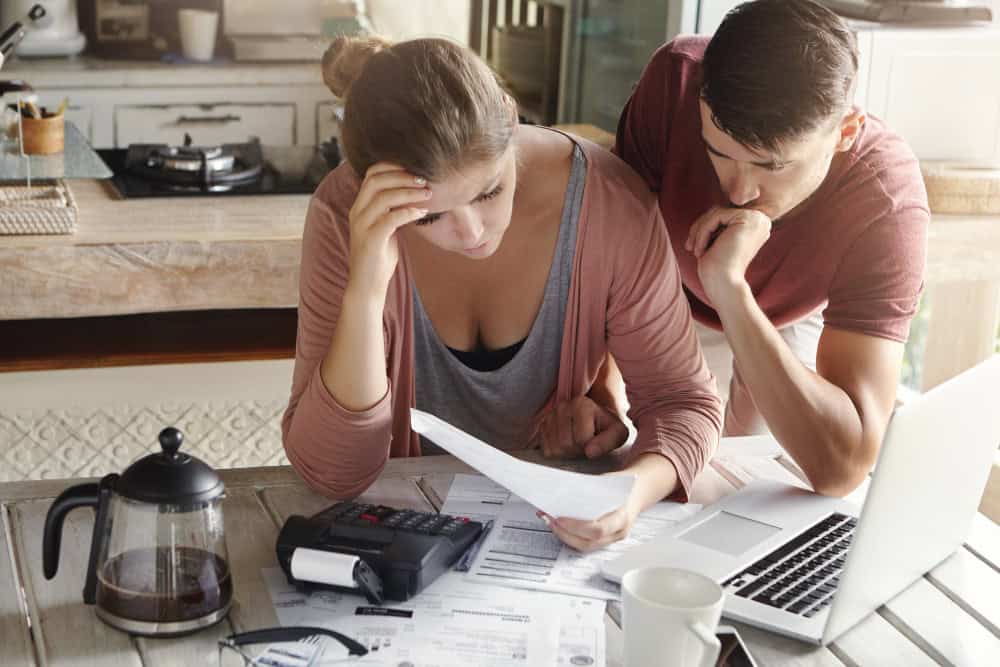 A couple sits at their table in their kitchen, looking at debt papers.