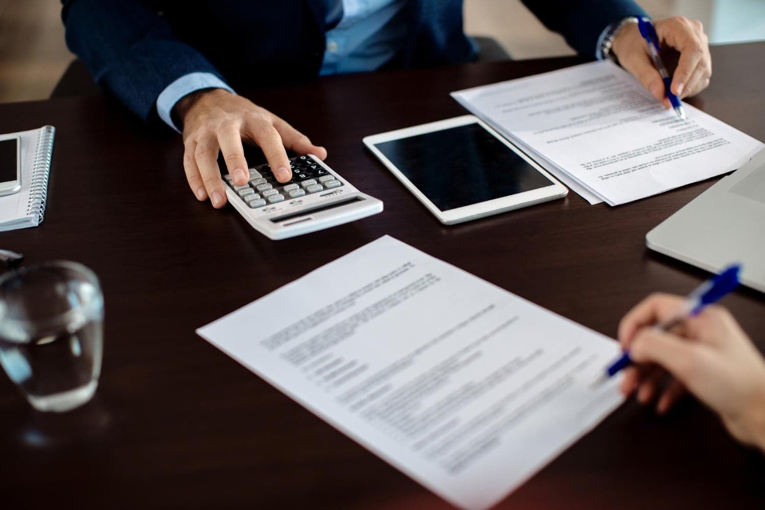 Business professionals reviewing legal documents and using a calculator at a desk.